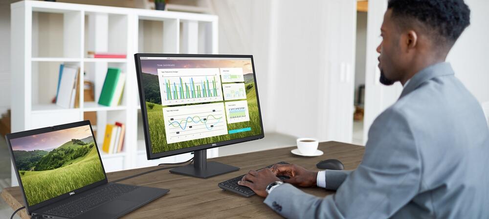 Imaginea unui barbat care foloseste produse Dell pe o masa, inclusiv un monitor Dell E2723, o tastatura si un mouse Dell si un laptop.