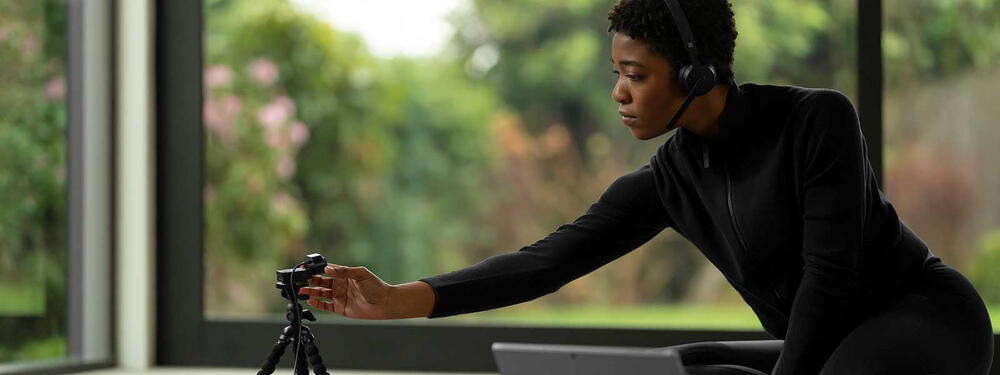 O femeie purtand o pereche de Microsoft Wireless headset ajusteaza o Microsoft Modern Webcam