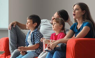 Familie se uita la televizor de pe o canapea