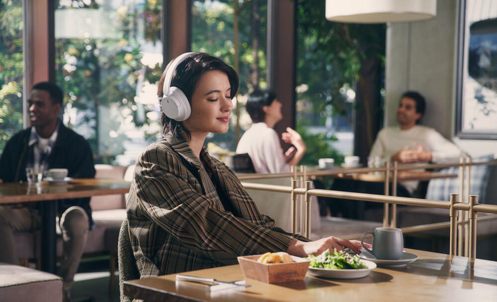 Imagine cu o femeie intr-un restaurant, bucurandu-se de muzica in timp ce foloseste o pereche de casti Sony WH-CH720 albe