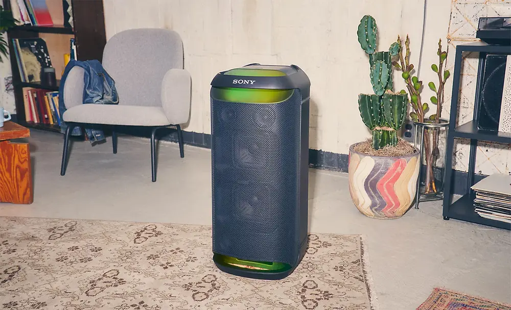 Imagine cu o boxa SRS-XV800 cu lumina ambientala verde, pe un covor intr-o camera, cu un scaun si un cactus