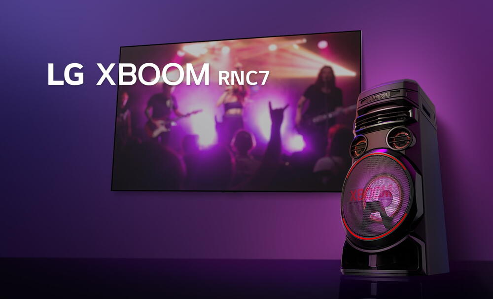 O vedere de jos a lateralei drepte a LG XBOOM RNC7 pe un fundal violet. Luminile XBOOM sunt, de asemenea, violet. Si un ecran TV afiseaza o scena de concert.
