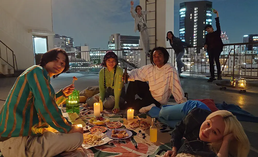Imagine cu un grup de persoane la un picnic pe acoperis, noaptea