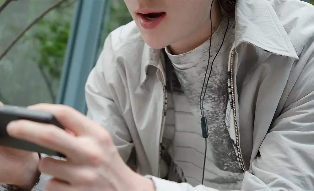 Prim-plan cu o persoana jucandu-se un joc pe Xperia 5 V, cu atentie pe microfonul unei perechi de casti cu fir
