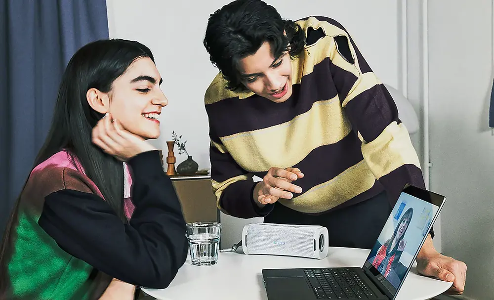 Doua persoane efectuand un apel video de pe laptop, folosind boxa portabila ULT FIELD 1 pentru sunet